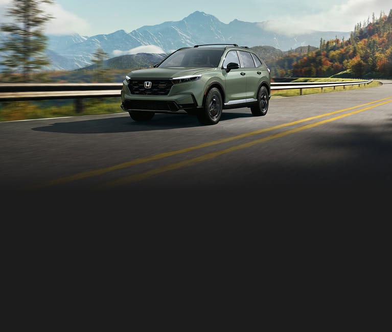 2026 Honda CR-V TrailSport Hybrid in Ash Green Metallic driving on a scenic mountain road (Compact Crossover SUV).
